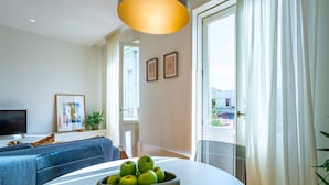 Een moderne woonkamer met een bank, een tafel met een schaal appels, een televisie en een groot raam met gordijnen.