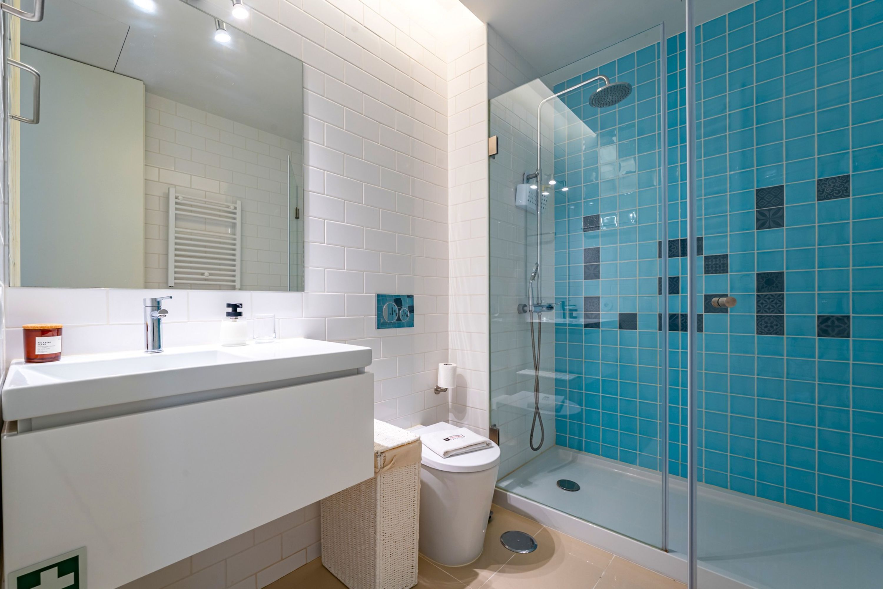 Ein Badezimmer mit einem weißen Waschbecken, einem Spiegel und einer Duschkabine mit blauen Fliesen.