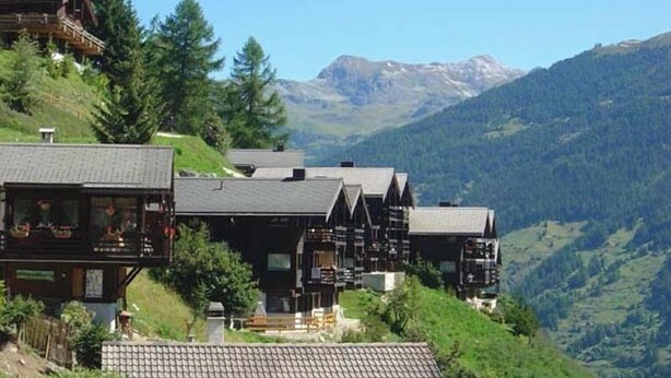 Un albergue de montaña con varias edificaciones de madera, un balcón y vistas de las montañas circundantes.
