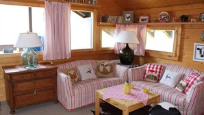 Interior acogedor de una cabaña con un sofá a rayas, una mesa de madera con mantel a cuadros y un aparador con cajones.