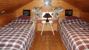 Un dormitorio acogedor en el ático con dos camas, paredes de madera, una mesita con lámpara y una ventana con cortinas.