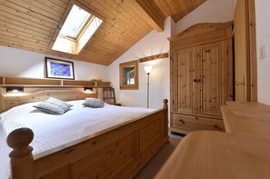 Ein Schlafzimmer mit Holzbalken, einem Oberlicht, einem Bett mit Kissen, einer Nachttischlampe und einem Kleiderschrank.