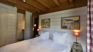 Een slaapkamer met een houten plafond, een bed met witte lakens, twee wandlampen en twee schilderijen van landschappen.