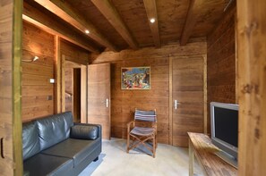 Ein Holzblockhaus-Interieur mit einem Ledersofa, einem gestreiften Sessel, einem Bild an der Wand und einem Fernseher auf einem Holzboden.