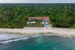 Hotel frente a la playa con piscina, rodeado de exuberante vegetación tropical.