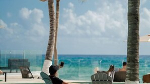 A beachside lounge with palm trees, a glass balustrade, and a view of the ocean. - The Beachfront by The Fives Hotels Á la Carte - Adults Only (Playa del Carmen)