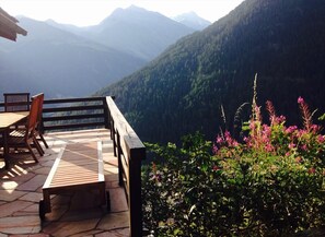 A wooden deck with a bench and chairs, overlooking a mountainous landscape with dense forests and flowering plants. - Very comfortable chalet for 6 persons : living room with wood stove - kitchen with dishwasher, micro (Grimentz)