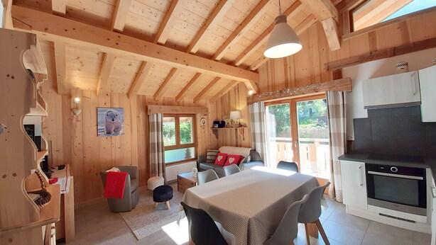 Interior de una cabaña de madera con comedor, cocina y un rincón de estar acogedor.