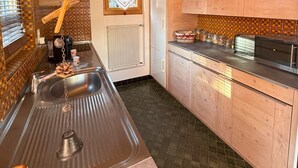 A kitchen with wooden cabinets, a stainless steel sink, and a window with a curtain. - Comfortable chalet for 5 persons : Living room with fireplace - kitchen with dishwasher, microwave a (Grimentz)