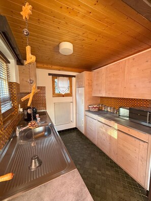 A kitchen with wooden cabinets, a stainless steel sink, and a window with a curtain. - Comfortable chalet for 5 persons : Living room with fireplace - kitchen with dishwasher, microwave a (Grimentz)