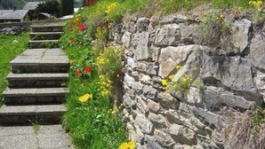 A stone staircase leading up a grassy slope with a stone wall on one side and a mountain view in the background. - Comfortable chalet for 5 persons : Living room with fireplace - kitchen with dishwasher, microwave a (Grimentz)