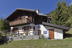 En traditionell chalet med en träbalkong, en grund av sten och en klocka på väggen.