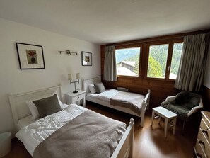 Ein Schlafzimmer mit zwei Betten, einem Sessel, einem kleinen Tisch und einem Fenster mit Vorhängen.