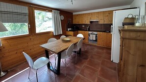Keittiössä on puiset kaapit, ruokapöytä tuoleineen, liesi ja jääkaappi.