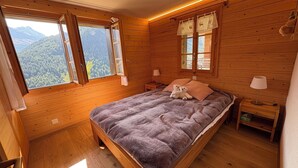 Camera da letto in una baita di legno, con un letto, un comodino, una lampada e una finestra con tende.