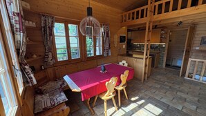 Un accogliente interno di una baita con zona pranzo, pareti in legno e cucina.