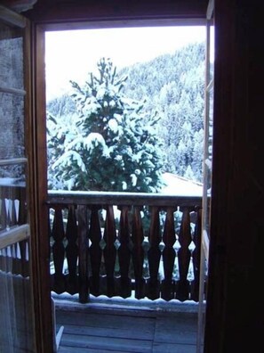 Un balcón de madera con barandilla de metal, con vista a un paisaje nevado con árboles.