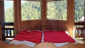 Ein Zimmer in einer Holzhütte mit zwei Betten, großen Fenstern und Blick auf einen bewaldeten Berg.