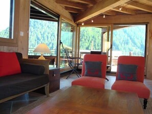 A cozy room with a wooden ceiling, a large window overlooking a forest, a sofa, two armchairs, and a table. - Chalet high standing close to the slopes for 12 persons : 1. floor : living-room with wood stove - k (Grimentz)