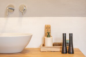 Ein Badezimmer mit einem großen, weißen Waschbecken, zwei schwarzen Flaschen, einer Holzbürste und einem Seifenspender.