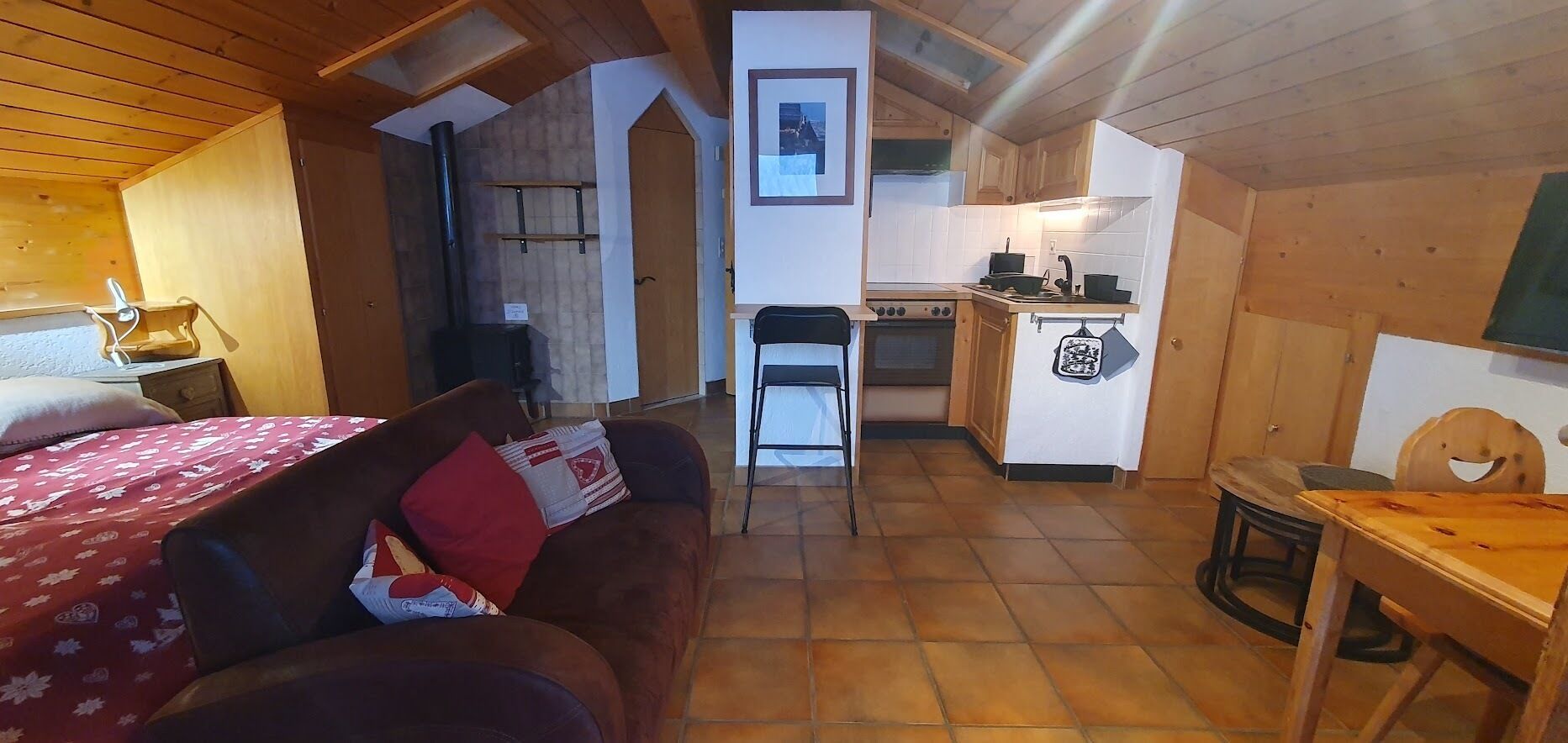 Ein gemütliches Zimmer mit einem Bett, einem Holztisch und einer Küchenzeile.