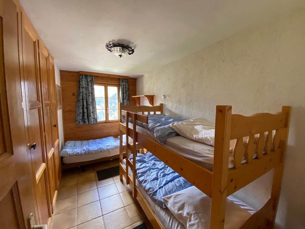 Une chambre avec des lits superposés, une armoire en bois et une fenêtre avec des rideaux.