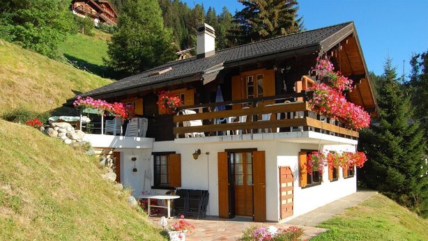 Ein Chalet mit Balkon, Steinstufen und einer kleinen Sitzecke im Freien.