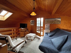 A cozy cabin room with a bed, a chair, a small table, a TV, and a window with a view of the mountains. - Very comfortable chalet for 6 persons: ground floor: living room with chimney - kitchen with dishwas (Grimentz)
