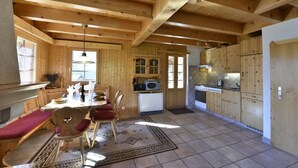 Een houten hut van binnen, met een eethoek, keuken en een groot raam.
