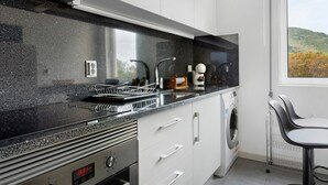 A kitchen with a black countertop, white cabinets, a built-in oven, and a window with a view of hills. - Apartment 'Machico Beach Front' with Sea View, Wi-Fi and Air Conditioning (Machico)