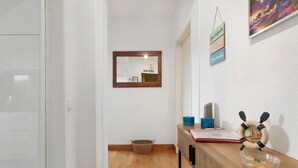 A hallway with a wooden floor, a mirror, a basket, a small table with a decorative item, and a wall-mounted sign. - Apartment 'Machico Beach Front' with Sea View, Wi-Fi and Air Conditioning (Machico)
