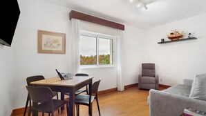 A modern living room with a dining area, a gray sofa, a wooden table, and a window with a view. - Apartment 'Machico Beach Front' with Sea View, Wi-Fi and Air Conditioning (Machico)