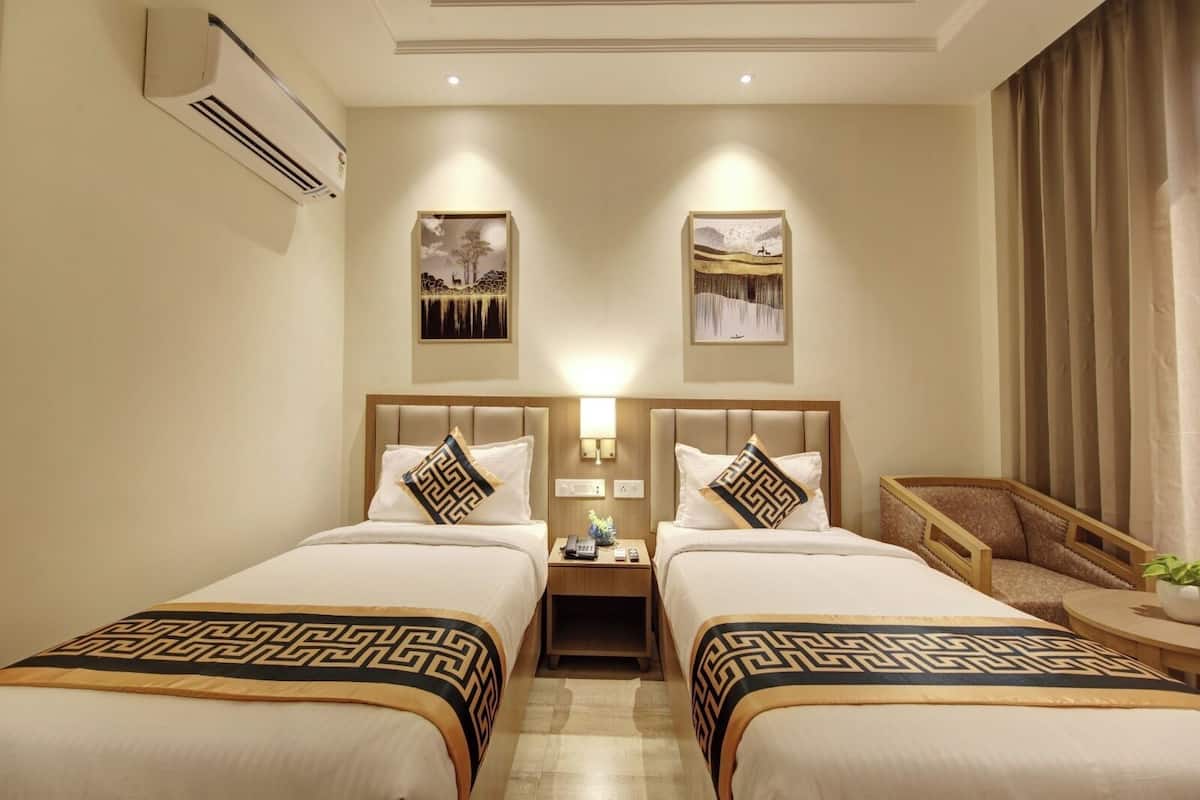 Habitación de hotel con dos camas, una mesita de noche con lámpara, una silla y obras de arte en las paredes.