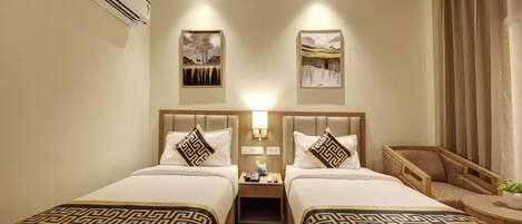 A hotel room with two beds, a nightstand with a lamp, a chair, and artwork on the walls.