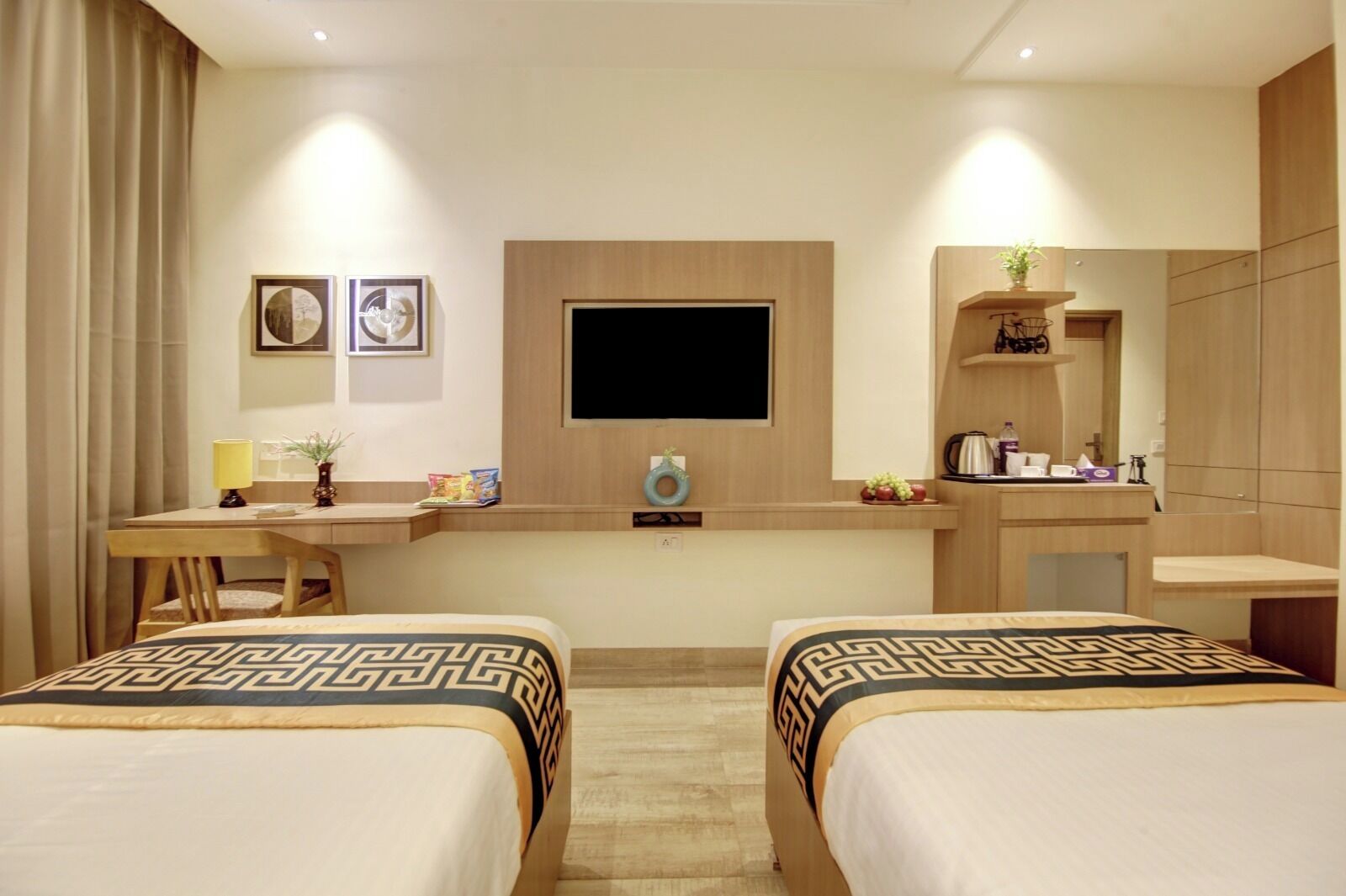 A hotel room with two beds, a desk, a TV, and a mirror.