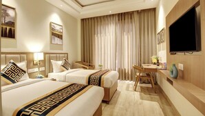 A hotel room with two beds, a desk, a television, and a large window with curtains.