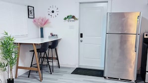 Ett modernt kök med ett kylskåp i rostfritt stål, en vit dörr och en klocka på väggen.
