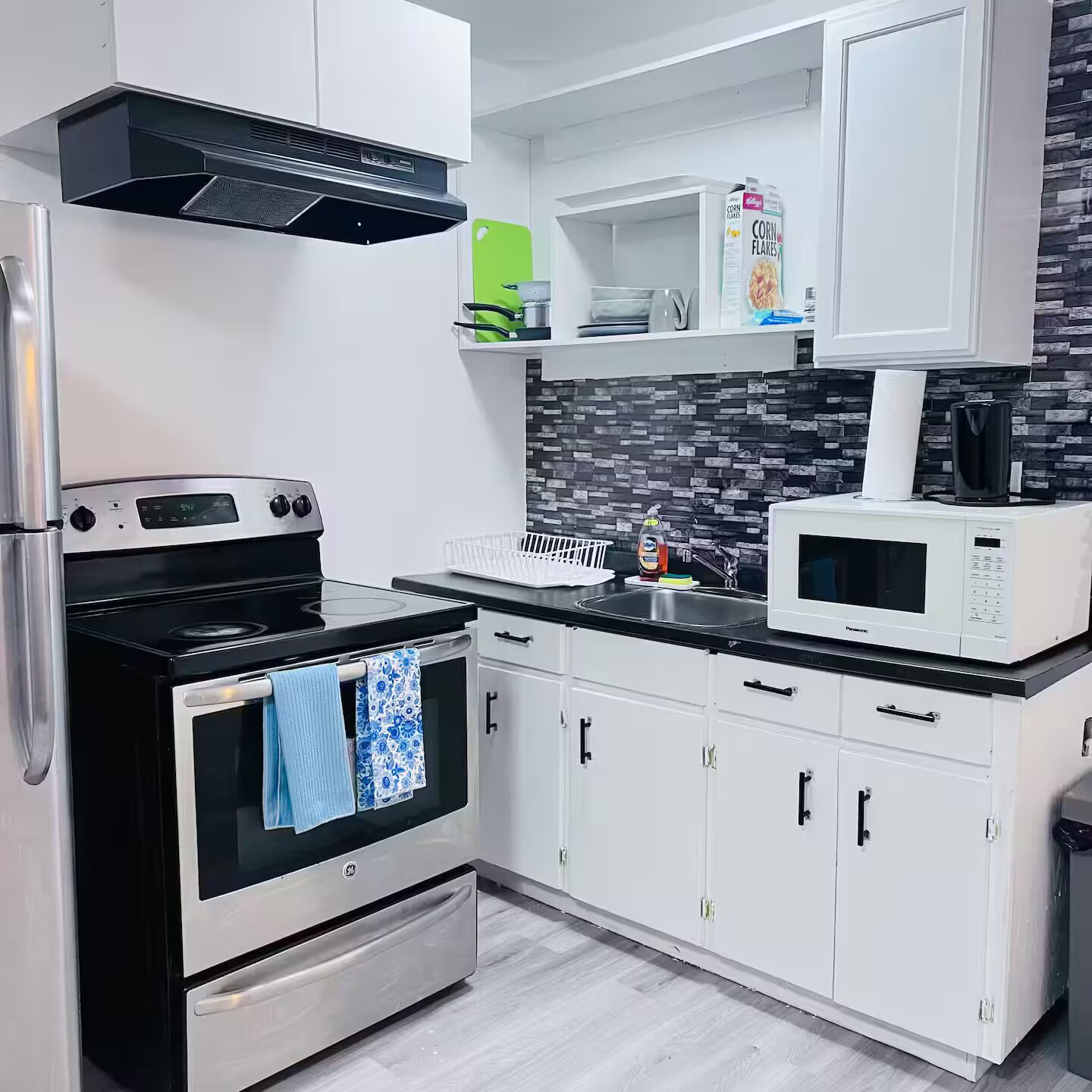 A modern kitchen with white cabinets, a black stove, a microwave, and a tiled backsplash.