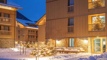 Un edificio de varios pisos con balcones, fachada de piedra y suelo cubierto de nieve.