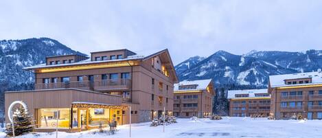 A modern hotel with multiple floors, balconies, and a snowy mountain backdrop.