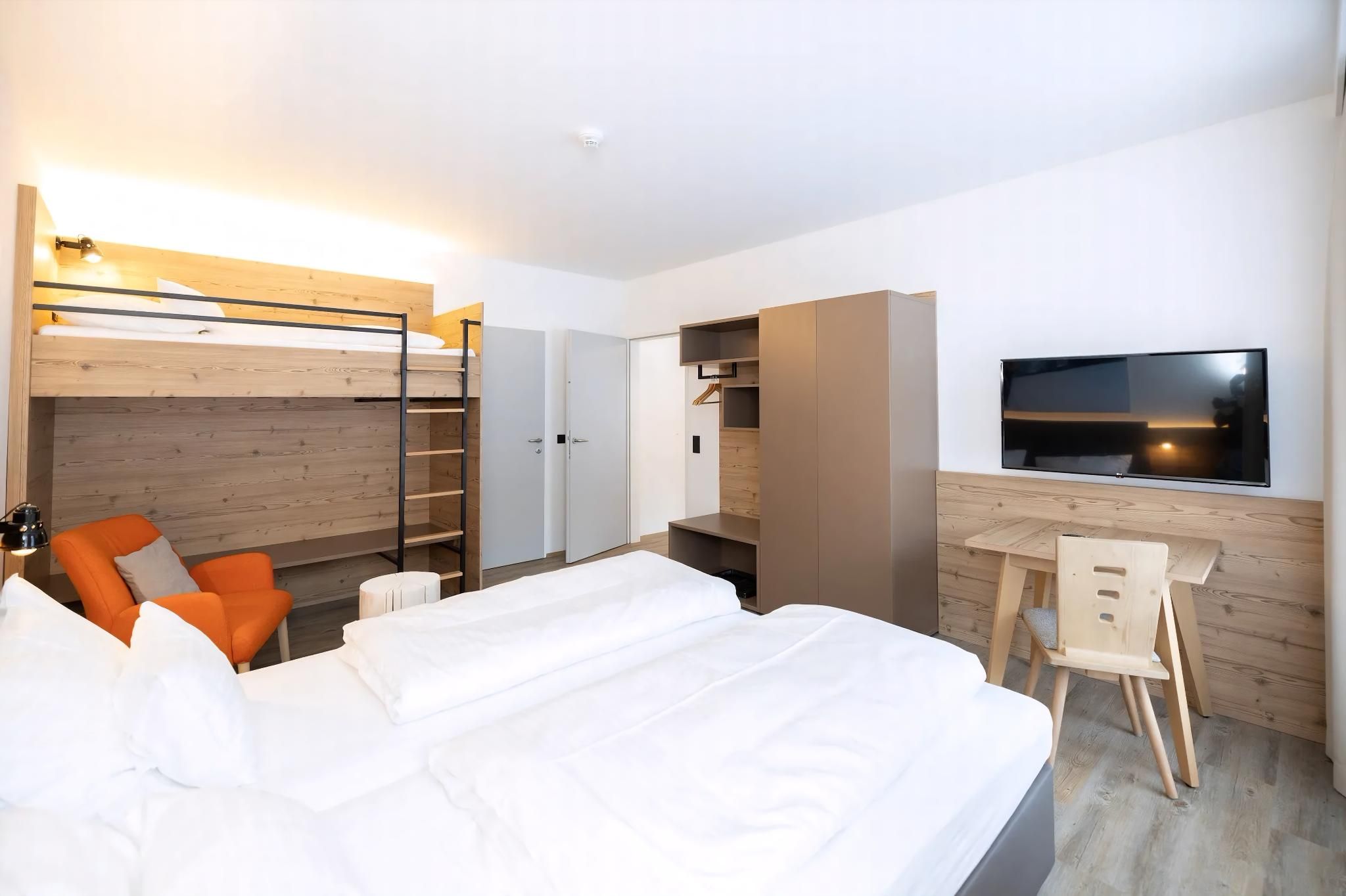 A modern hotel room with a large bed, a desk with a chair, a TV, and a wardrobe.