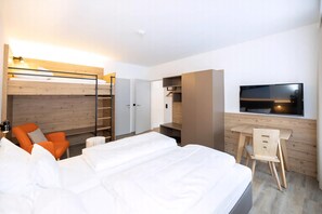 A modern hotel room with a large bed, a desk with a chair, a TV, and a wardrobe.