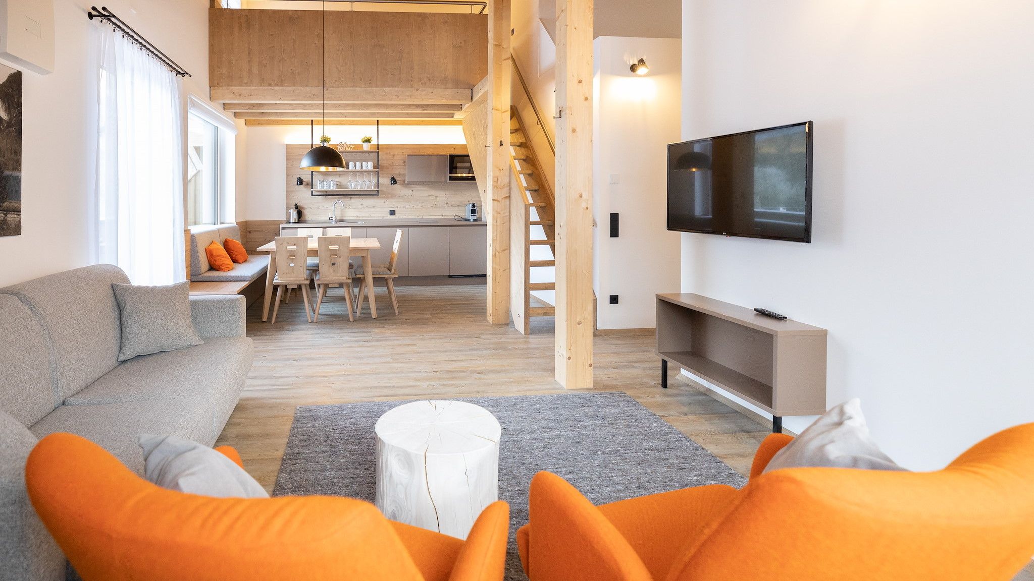A modern living room with a sofa, orange cushions, a coffee table, and a TV.