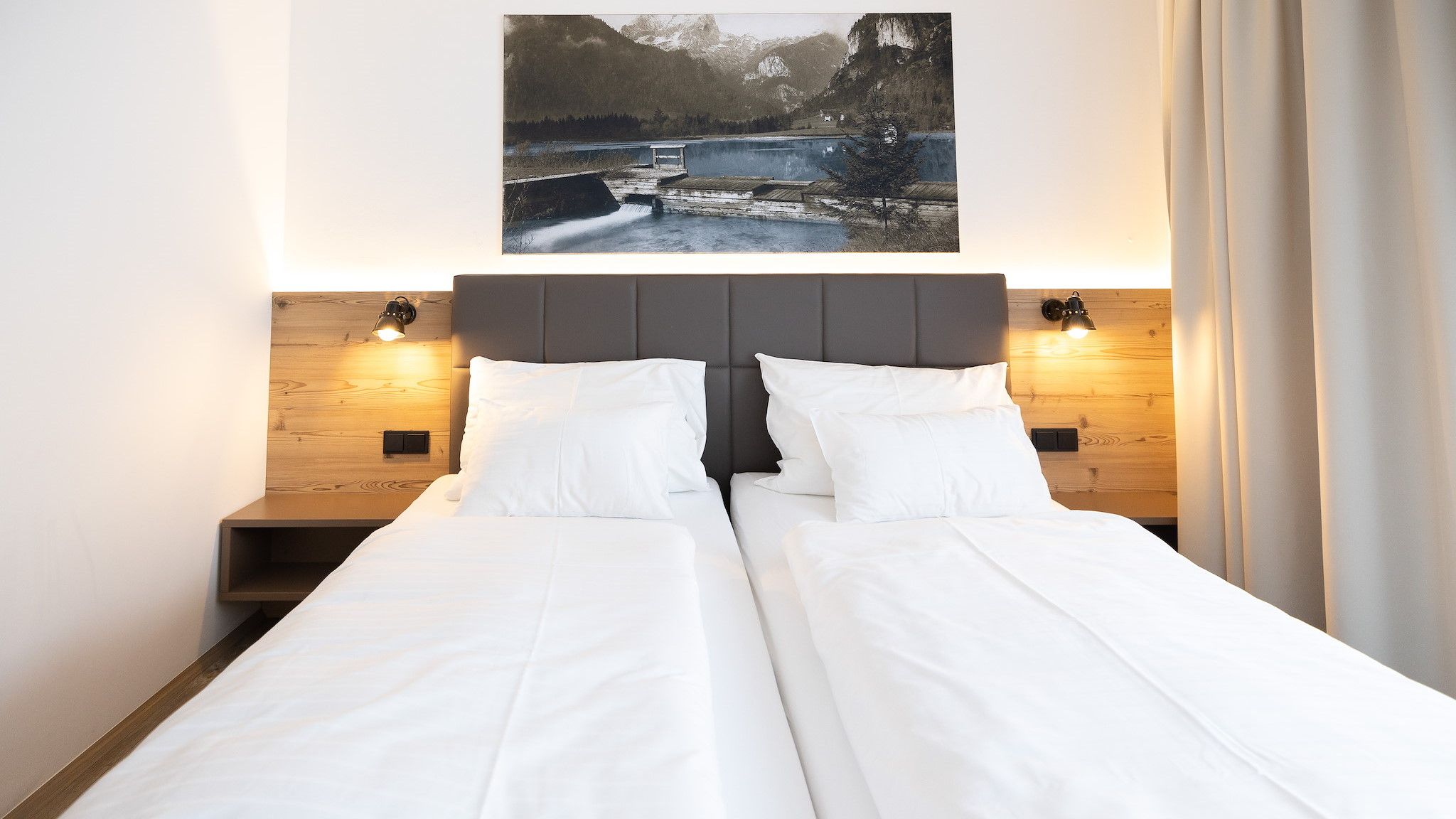 Cama doble con cabecera de madera y dos mesitas de noche con lámparas.