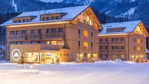 Ein mehrstöckiges Hotel mit Balkonen, einer Skiliftanlage und einem verschneiten Berg im Hintergrund.
