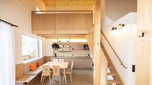 A modern kitchen with wooden cabinetry, a dining area with a bench and chairs, and a staircase leading to an upper level. - Dormio Aparthotel Hinterstoder (Hinterstoder)