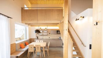 Eine moderne Küche mit Holzschränken, ein Essbereich mit einer Bank und Stühlen sowie eine Treppe, die zu einer oberen Ebene führt.