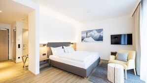 Ein modernes Hotelzimmer mit einem großen Bett, einem Flachbildfernseher, einem Sessel und einem Bild an der Wand.