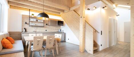 Una cocina moderna con armarios de madera, un comedor con mesa y sillas, y una escalera que lleva a otro nivel.