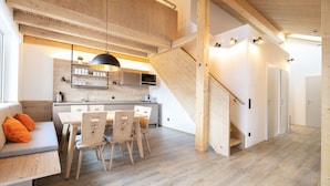 A modern kitchen with wooden cabinetry, a dining area with a table and chairs, and a staircase with a wooden railing. - Dormio Aparthotel Hinterstoder (Hinterstoder)